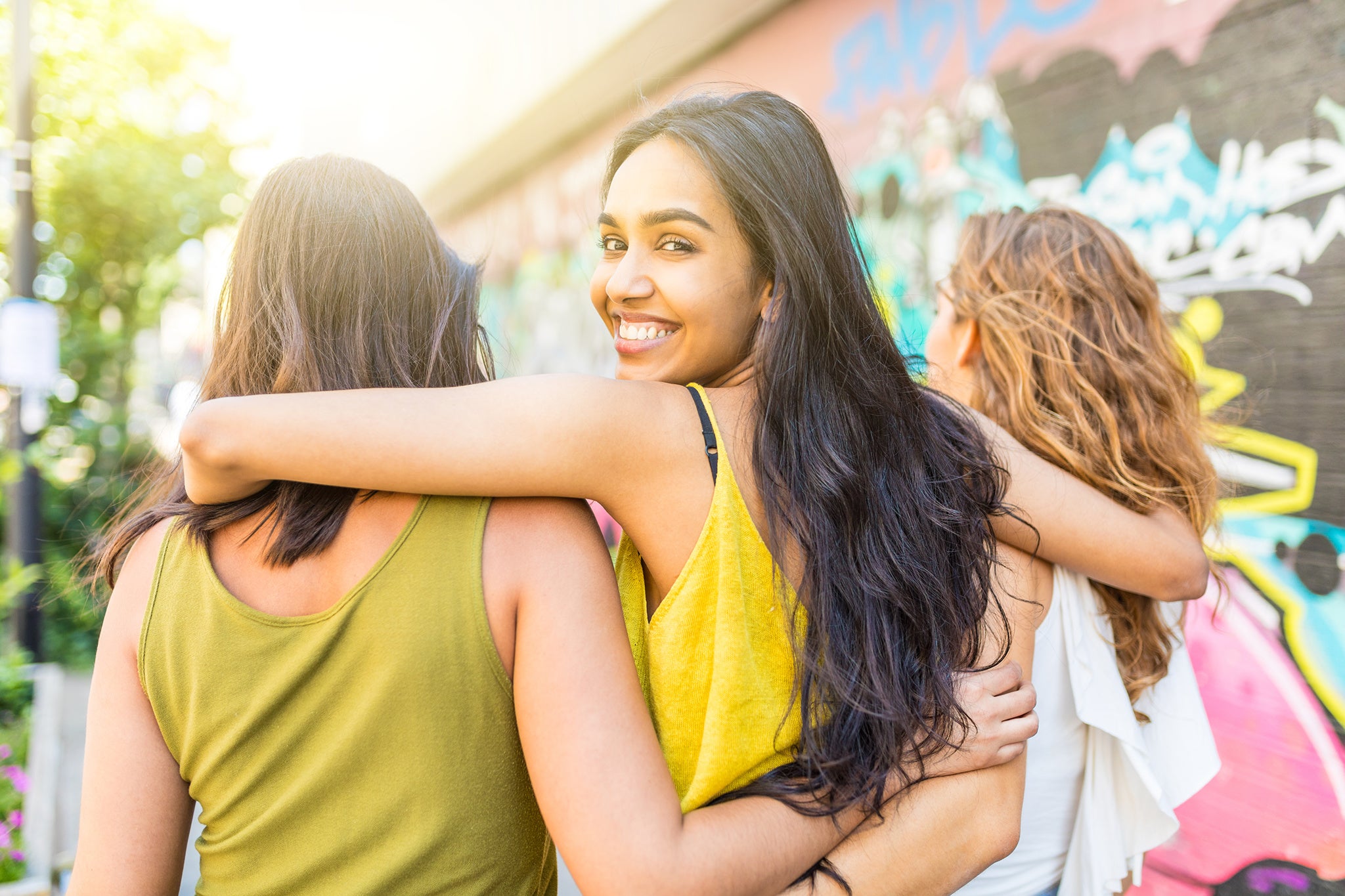 Beautiful woman embracing girl friends walking in the city - Urban portrait of a mixed race young woman looking back at camera and smiling - Diversity and lifestyle concepts in multicultural London city