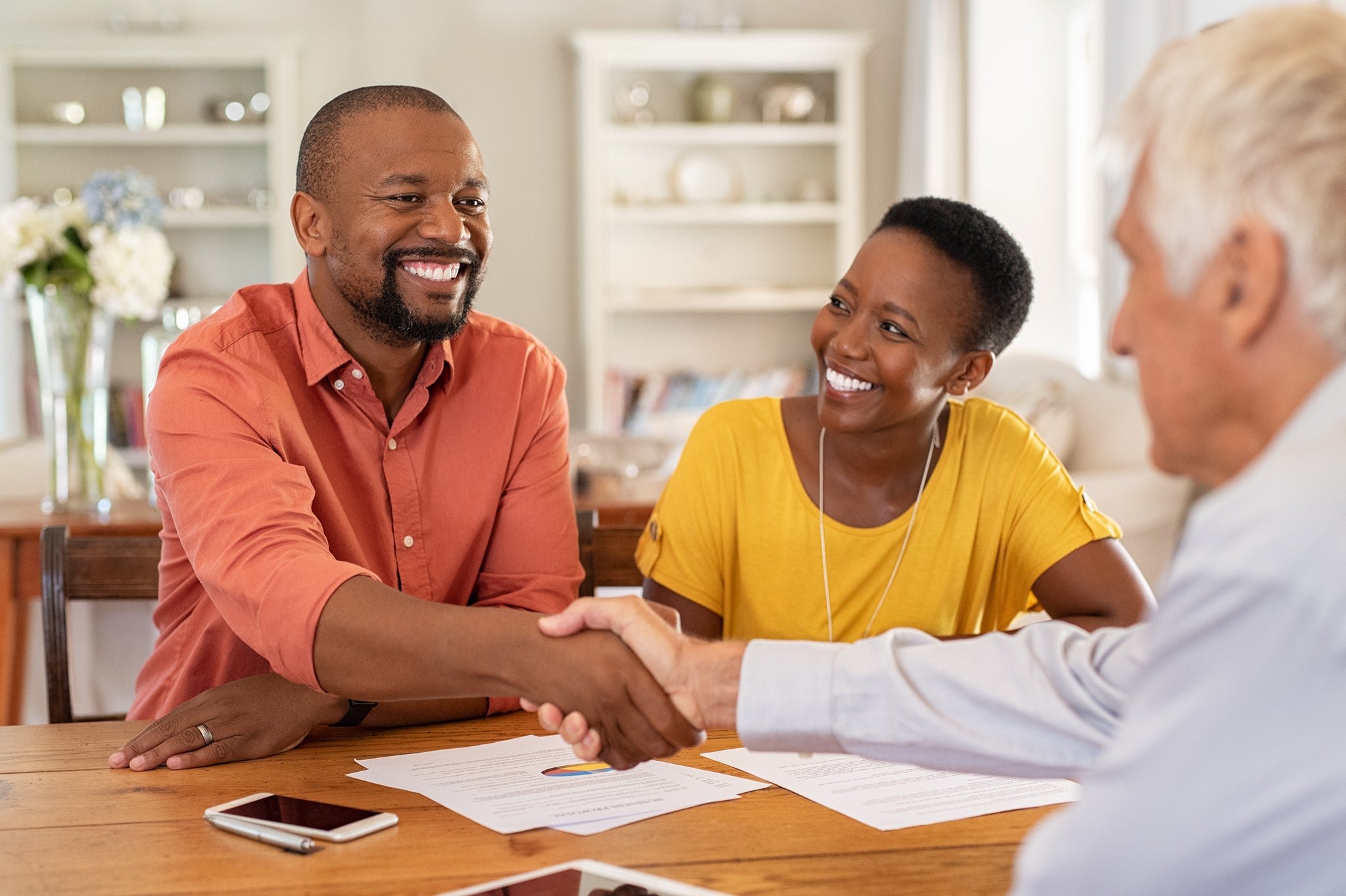 Mature black husband shaking hands with senior agent on taking loan. Happy african couple sealing with handshake a contract with financial advisor for investment. Man making sale purchase deal concluding with a handshake with estate agent.