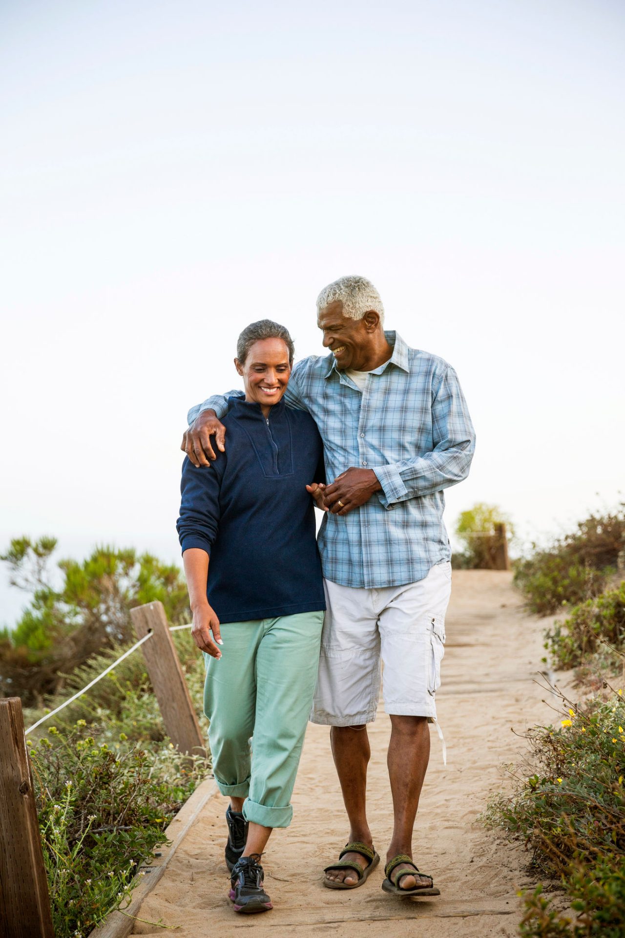 Senior african american couple casually dressed walking together on a boardwalk outdoors near the beach.