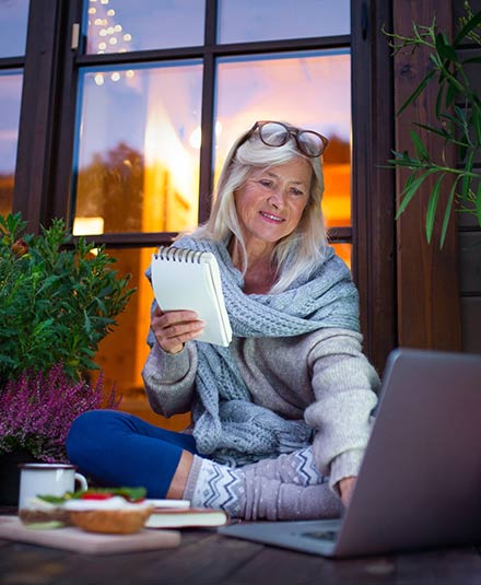 A woman sitting on her patio learns about survivor benefits for widows on her laptop.